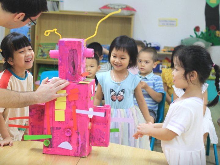 Children and their teacher looking at a robot they built from boxes